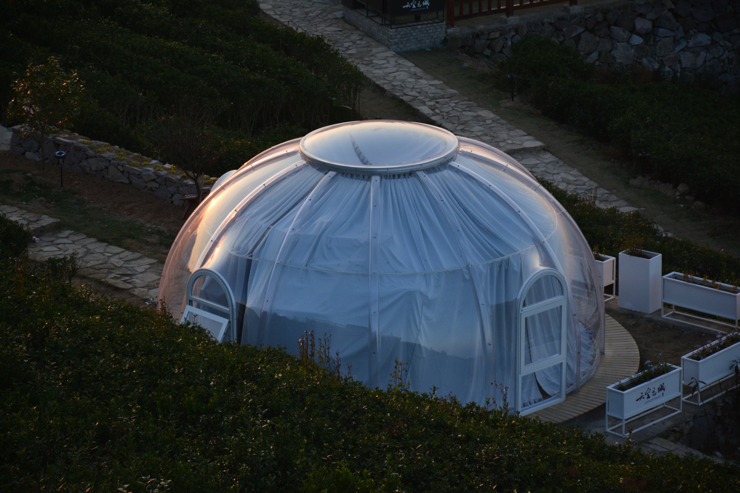 Large polycarbonate transparent Dome-shaped building at night with a pathway leading to it. Polycarbonate domes are sold by Glamping Dome Store.
