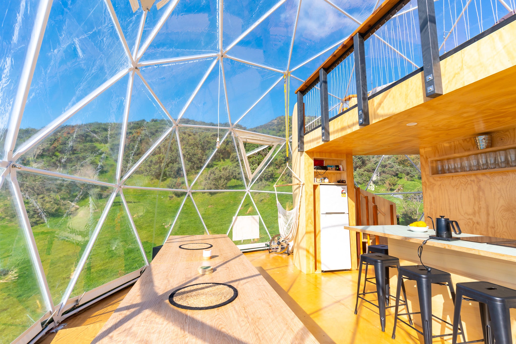Geodesic dome structure with an interior view of a kitchen and outdoor scenery. The dome was designed by Glamping Dome Store.
