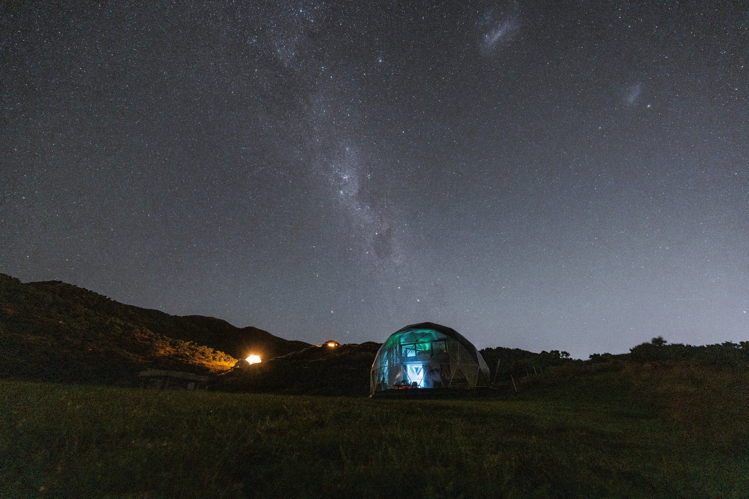 Starry night sky over a dome-shaped structure in a grassy field in New Zealand. Project of Glamping Dome Store.