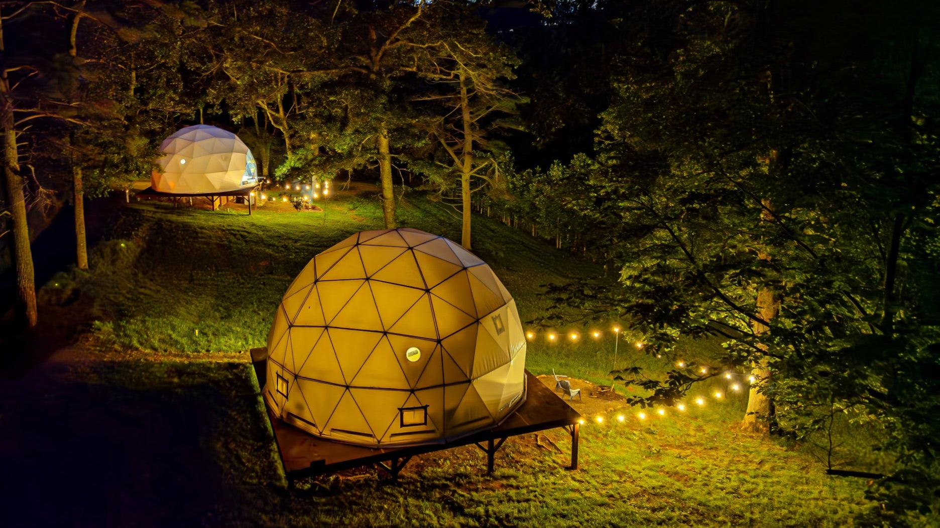 Geodesic dome tents in a North Carolina forest setting with string lights at night. Project domes were designed and manufactured by Glamping Dome Store.