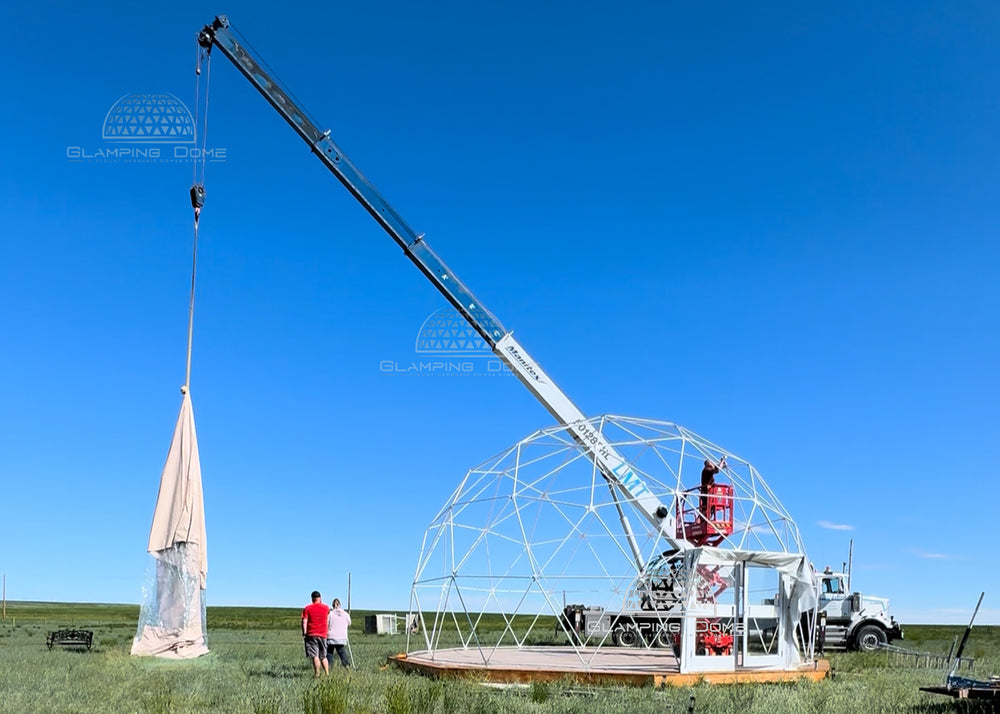 Geodesic dome new replacement cover being lifted by a crane in an open field with a clear blue sky.