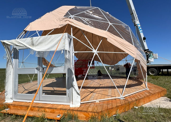 Geodesic dome structure with transparent walls on a grassy field under a clear blue sky.