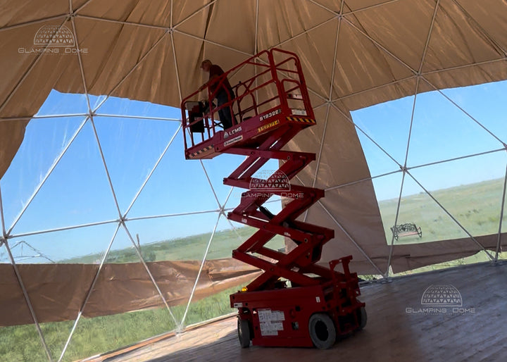 Red scissor lift inside a large geodesic dome structure with a person on top adjusting new dome tent pvc cover