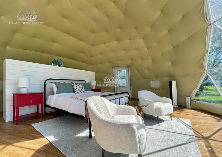 Interior of a 23-foot (7-meter) geodesic dome tent kit, a project by Glamping Dome Store, located at Maison des Prés with Dome & Jacuzzi in Saint-Basile-le-Grand, Quebec, Canada. This luxurious glamping space features a comfortable bed with plush bedding, bright red nightstands, modern armchairs, and a glass coffee table. The soft tufted insulation and spacious design create a cozy yet elegant atmosphere, ideal for a relaxing outdoor retreat.